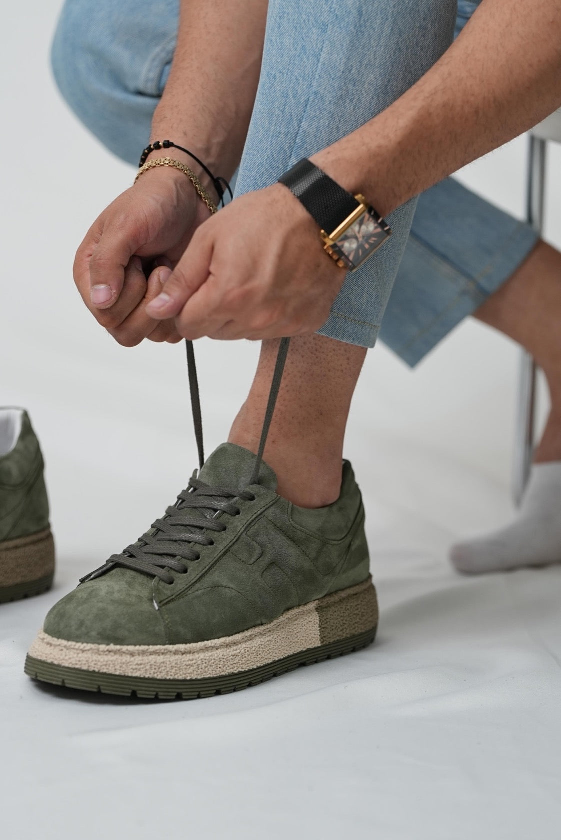 Person tying the laces of a green sneaker on a light background