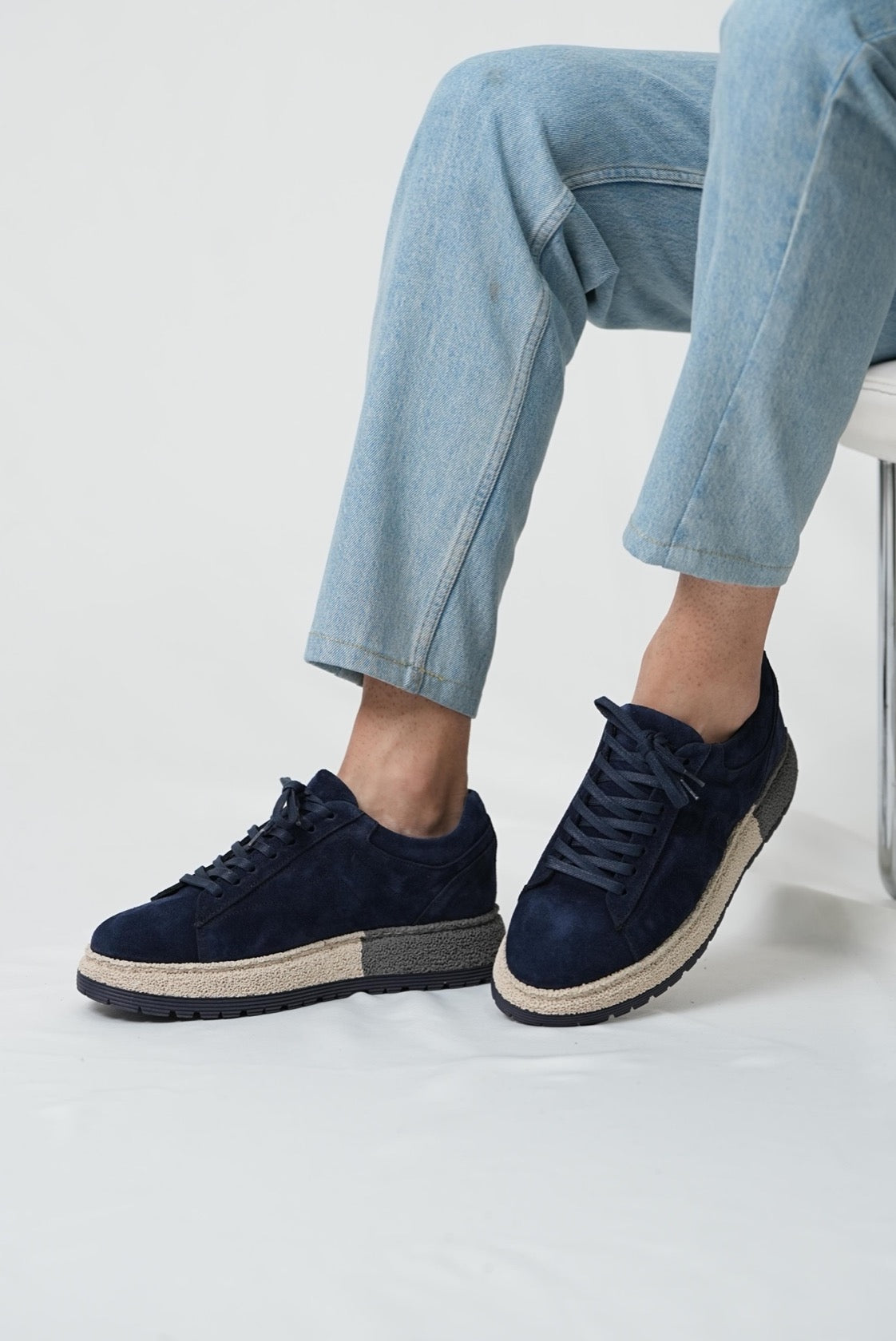 Navy blue sneakers worn with light blue jeans on a white background
